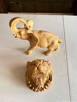 Elephant figurine and lion head plaque on table showing overall form and finish