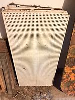 Stack of perforated metal pegboard panels leaning against wall