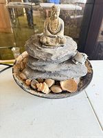 Overall view of fountain showing Buddha figure, stacked rocks, bowl with pebbles and shells, cord visible