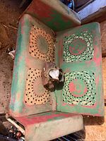 Top view of metal porch glider showing perforated seat and back panels, layered paint, rust, and small object resting on seat