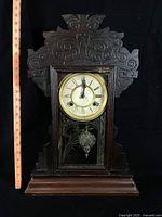 Front view of carved wooden mantel clock showing dial, door and overall design