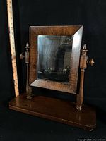 Front view showing mirror, wooden frame, turned supports, base and bun feet