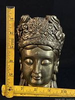 Front view of brass goddess head with ruler for scale showing about 6 in height