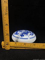 Lidded porcelain box measured with ruler showing diameter and height