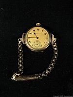 Closed Elgin pocket watch with attached link bracelet on black background