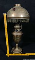Full view of assembled brass oil lamp with shade, measuring tape for scale