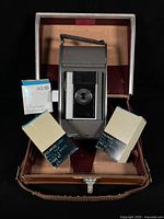 Camera standing in open case with film and flashbulb boxes visible