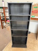 Front view of one black wood five-shelf unit showing overall structure and shelf count