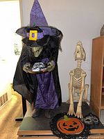 Witch figure beside skeleton dog, pumpkin cutout and mask visible