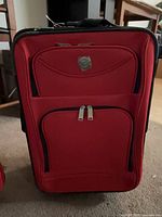 Front view of red soft-sided rolling suitcase with Travelers Club badge