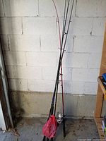 Four fishing rods leaning against wall, red plastic bag covering reel area