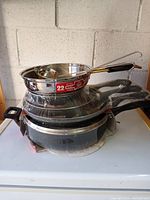 Stack of stainless and black frying pans, ladle visible