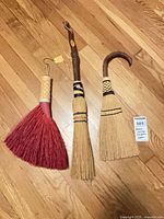 Full view of three handheld brooms on hardwood floor