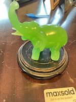 Front view of jade green pressed glass elephant figurine on black wooden base