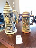 Front view of both steins showing size difference and relief scenes