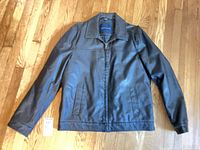 Front view of black faux leather jacket laid flat showing collar, zipper, pockets, hang tag visible