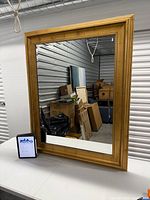 Full view of gold framed mirror leaning against wall, boxes reflected