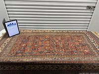 Full view of Caucasian rug on table with MaxSold tablet for scale