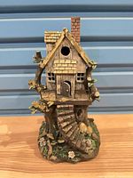 Front view of ceramic fairy house showing doorway, window, stairs and decorative foliage