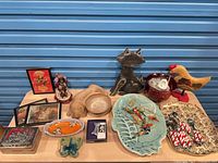Overview of assorted items on tabletop including framed art, figurines, dishes and utensils