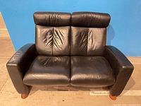 Front view of black leather two-seat recliner loveseat with wood feet