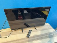 Front view of RCA 32" TV on stand with two remotes