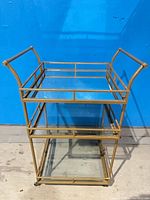 Full view of bar cart showing metal frame, two glass shelves, and casters