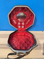 Case opened displaying red quilted interior, mirror, two bottles, and exterior strap visible