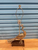 Full view of brass peacock lamp with harp on wooden base