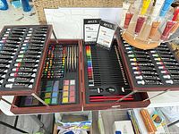 Open Art 101 wooden case showing paints, pencils, pastels, brushes; paint wheel with leather paint tubes adjacent