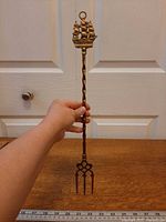 Full length view of brass toasting fork against ruler for scale