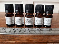 Five amber beard-oil bottles lined up with ruler