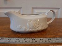 Side view of gravy boat showing turkey relief, handle and spout with ruler for scale