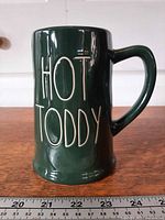 Left side view of green Rae Dunn mug showing "HOT TODDY" text and ruler for scale