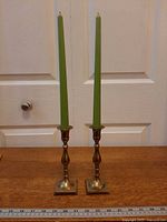 Full view of both brass candlesticks with green taper candles and ruler for scale