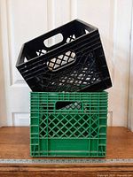 Black crate stacked diagonally atop green crate showing lattice sides and handles