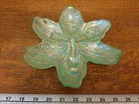 Top view of green iridescent flower-shaped dish with ruler for scale