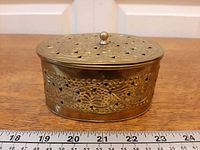 Front view of oval pierced brass box with ruler for scale
