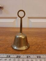 Full view of brass bell standing upright beside ruler