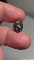 Oval cabochon black opal on fingertips showing multicolor play