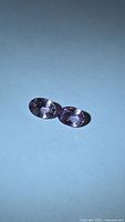 Pair of oval purple-pink spinel gemstones on neutral background