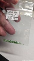 Small resealable bag containing multiple green round faceted gemstones with handwritten label detailing weight and size