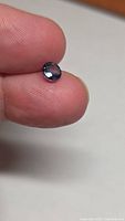 Round blue sapphire on fingertip showing size and color