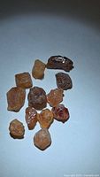 Group of 13 orange to reddish rough crystals on white background