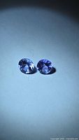 Both tanzanite gemstones side by side under spotlight
