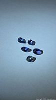 Five blue-violet tanzanite gemstones on neutral background