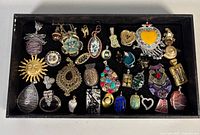Overall view of 25 assorted costume pendants and pins in tray