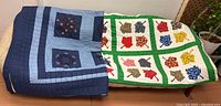 Both quilts displayed folded on bed showing patterns and colours