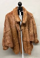 Front view of light brown rabbit fur coat on hanger