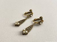 Pair of gold-tone filigree clip-on drop earrings with faux pearl clusters displayed flat
